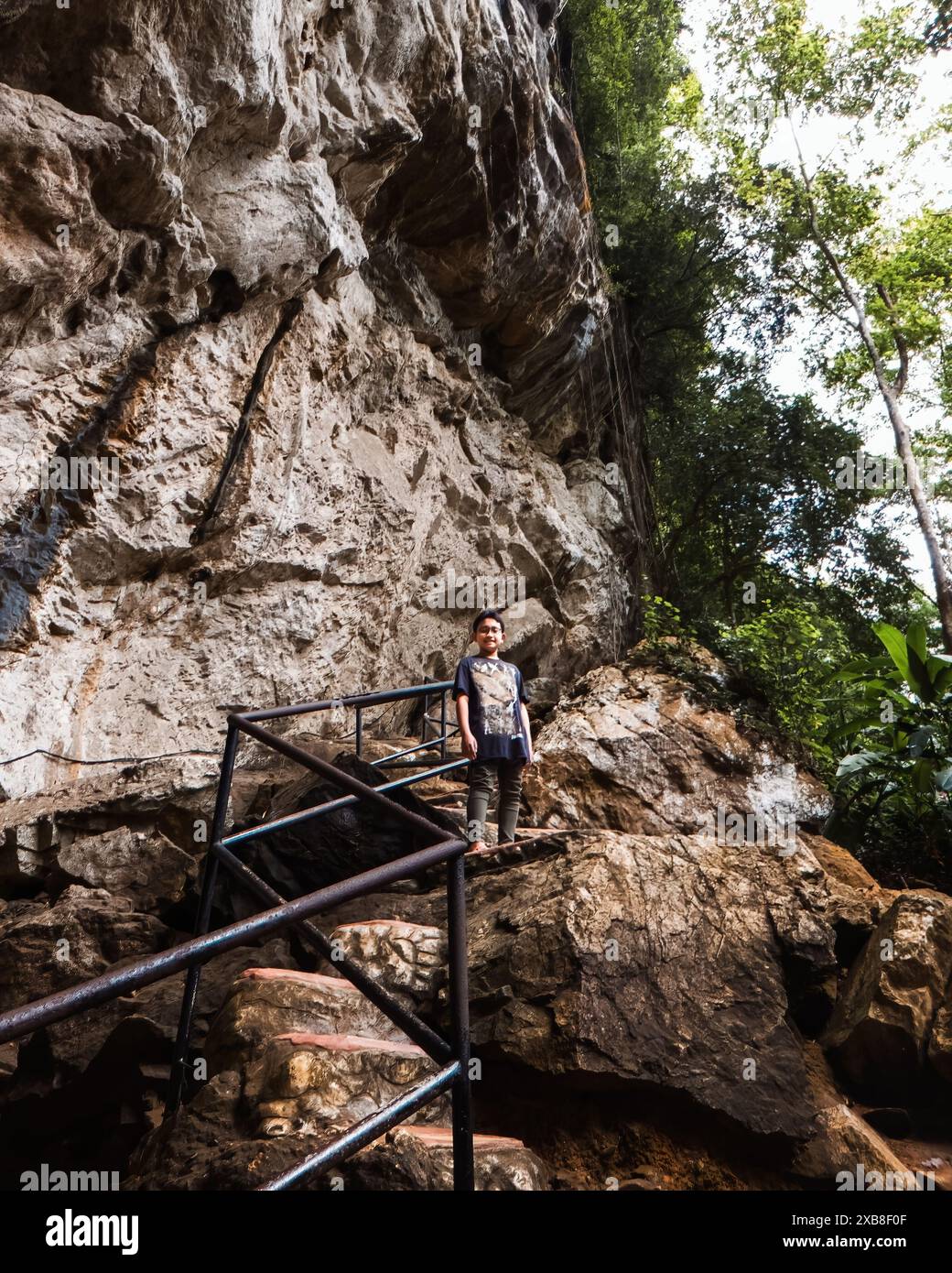 Ein kleiner Junge steht an der natürlichen Treppe der Berghöhle im Regenwald in Malaysia. Stockfoto