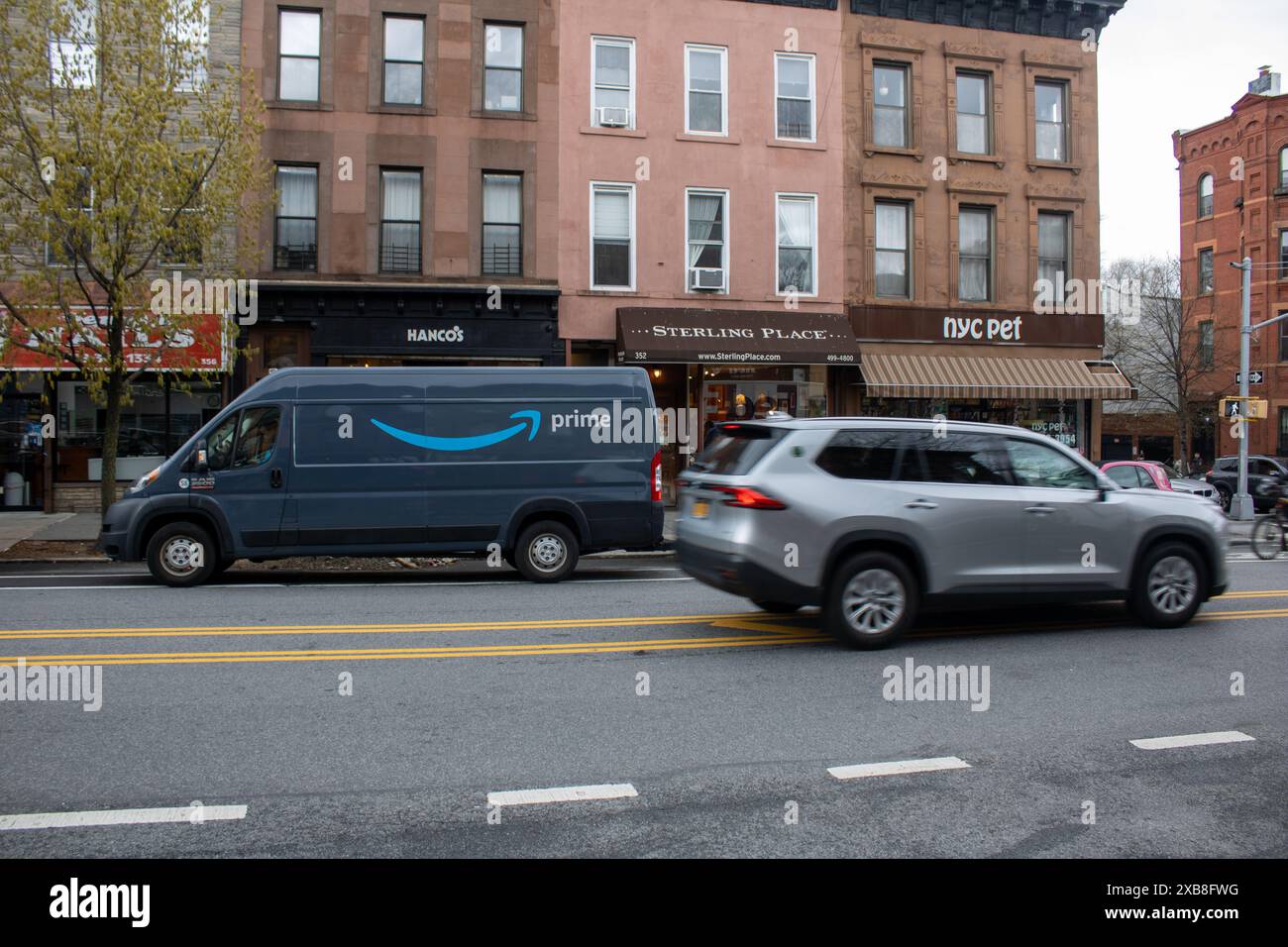 Die beiden Autos fahren auf der Stadtstraße in der Nähe von Geschäften in New York, USA Stockfoto