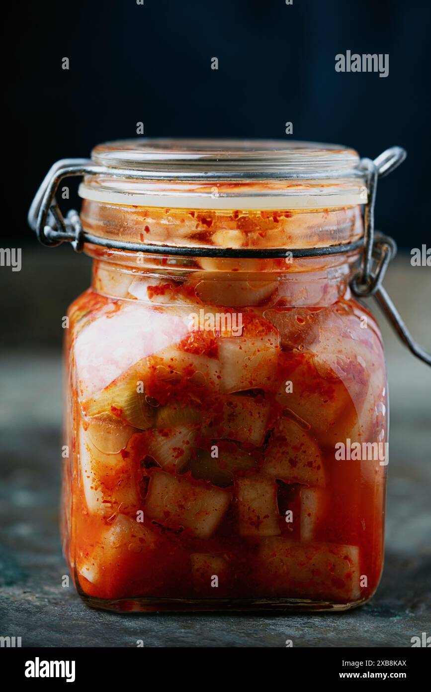 Glasgefäß gefüllt mit traditionellem koreanischem Rettich Kimchi Kkakdugi, einem scharfen und fermentierten Rettich, auf einem rustikalen dunklen Hintergrund. Stockfoto