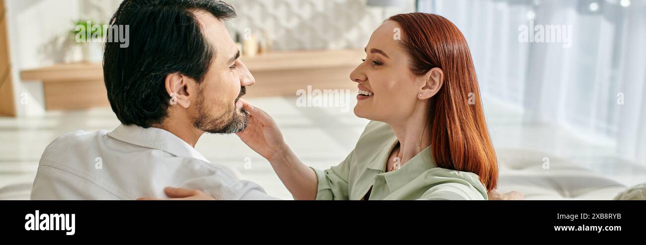 Eine rothaarige Frau und ein bärtiger Mann teilen einen zärtlichen Moment, während sie einander in die Augen blicken. Stockfoto