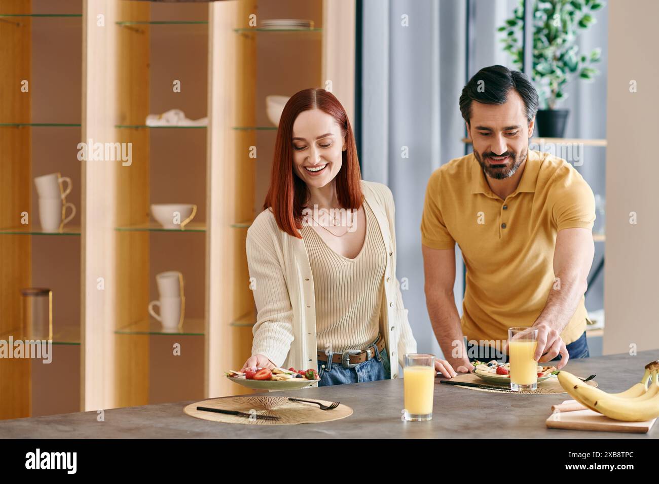 Eine rothaarige Frau und ein bärtiger Mann bereiten Zutaten zu und kochen zusammen in einer modernen Wohnküche. Stockfoto