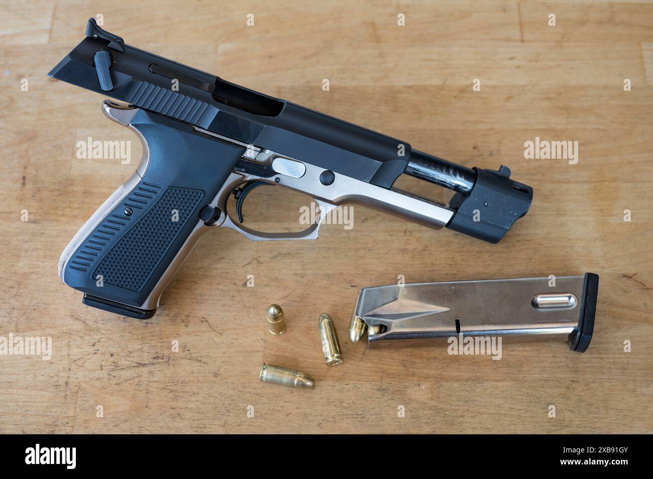 Detail einer schönen offenen und entladenen 9-mm-Polizeipistole neben einem geladenen Kugelmagazin und ein paar Kugeln auf dem Holztisch Stockfoto