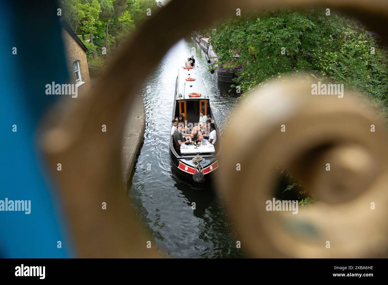 Menschen auf einem Boot werden hinter Geländern gesehen, während sie den warmen Sonnenschein in Little Venice, London, genießen. Stockfoto