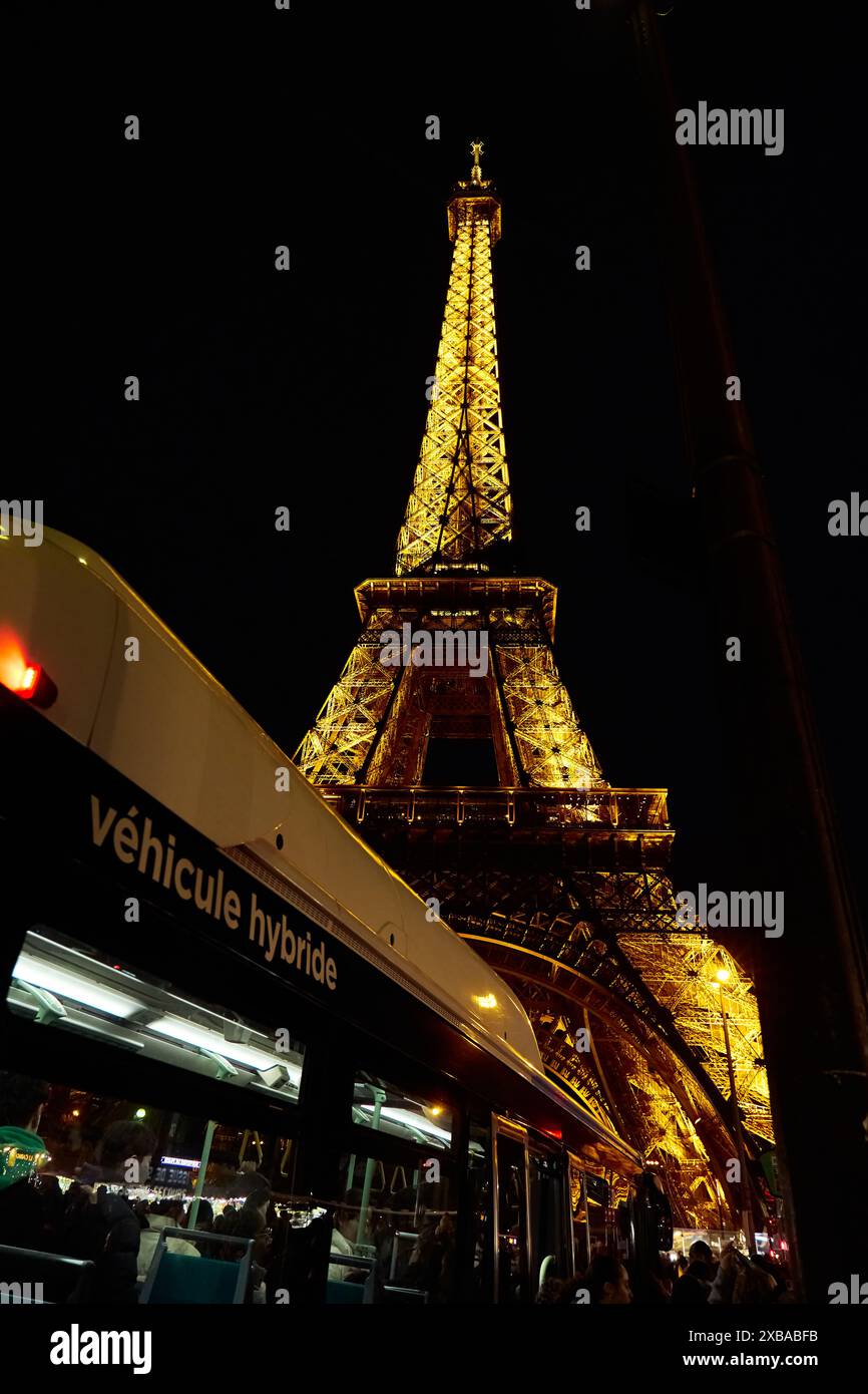 Ein hybrider öffentlicher Bus fährt bei Nacht an der Eiffeltour in Paris vorbei Stockfoto