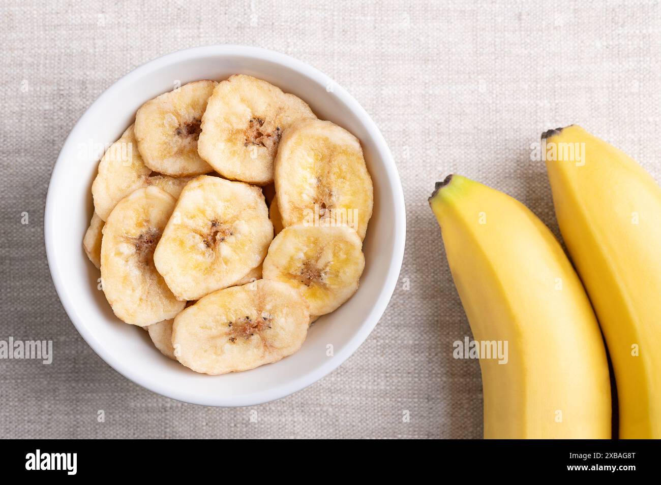 Bananenchips oder Bananenchips in einer weißen Schüssel auf Leinenstoff. Gelbe knusprige, frittierte Bananenscheiben, bedeckt mit Zucker oder Honig. Stockfoto