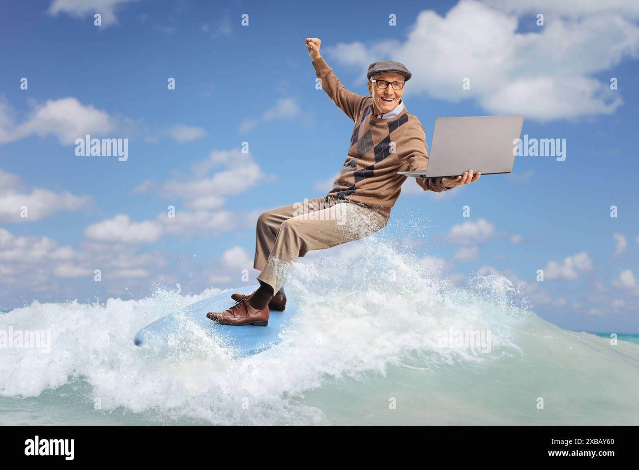 Ein älterer Mann, der auf einer Welle im Meer auf einem Surfbrett reitet und einen Laptop hält Stockfoto