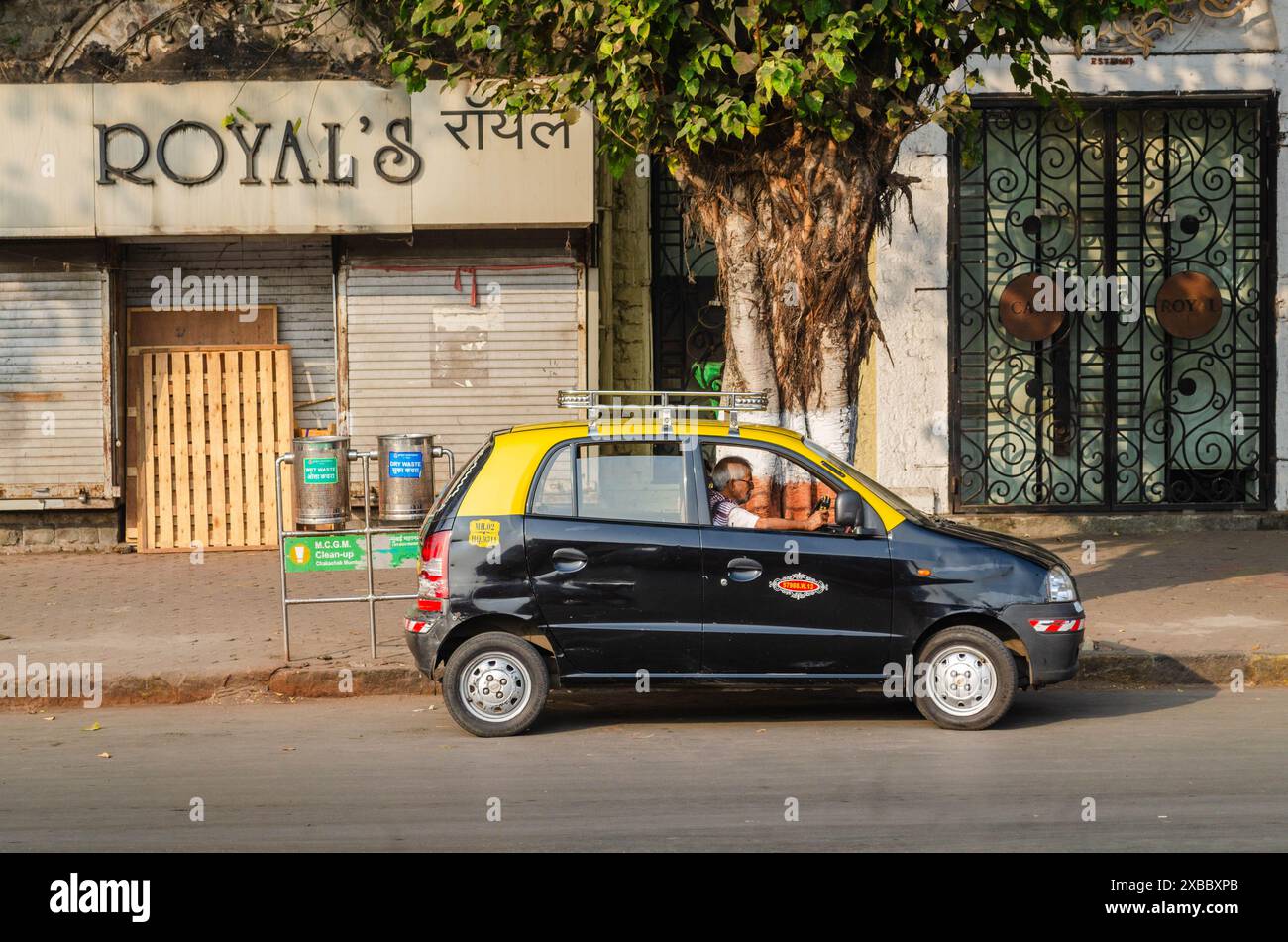 Ein Taxifahrer, der in einem gelben und schwarzen Taxi in Mumbai, Indien, Zeitung liest Stockfoto