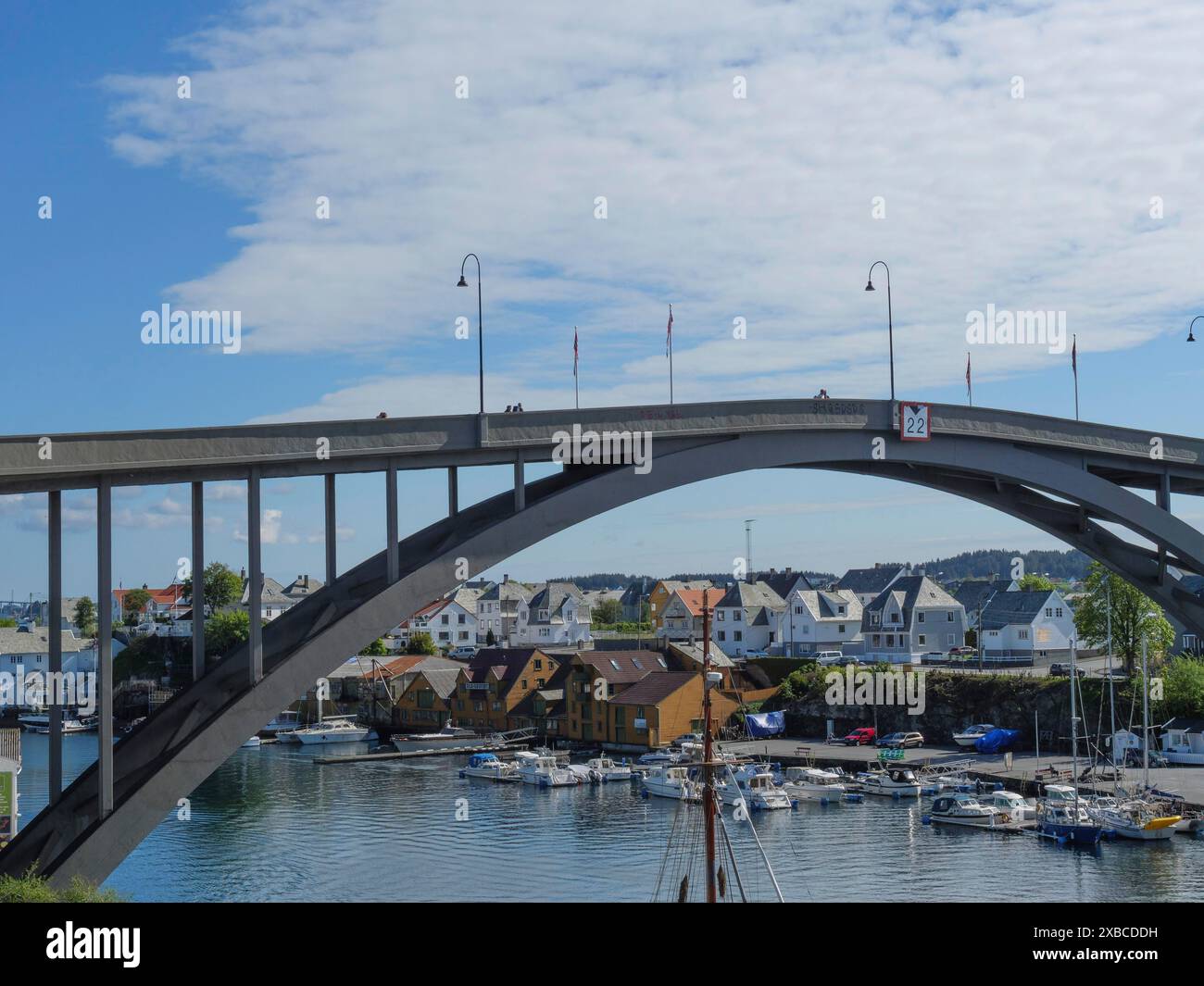 Hafenstadt mit Brücke über einen Kanal und kleinen Booten in der Nähe von Häusern unter leicht bewölktem Himmel, haugesund, norwegen, skandinavien Stockfoto
