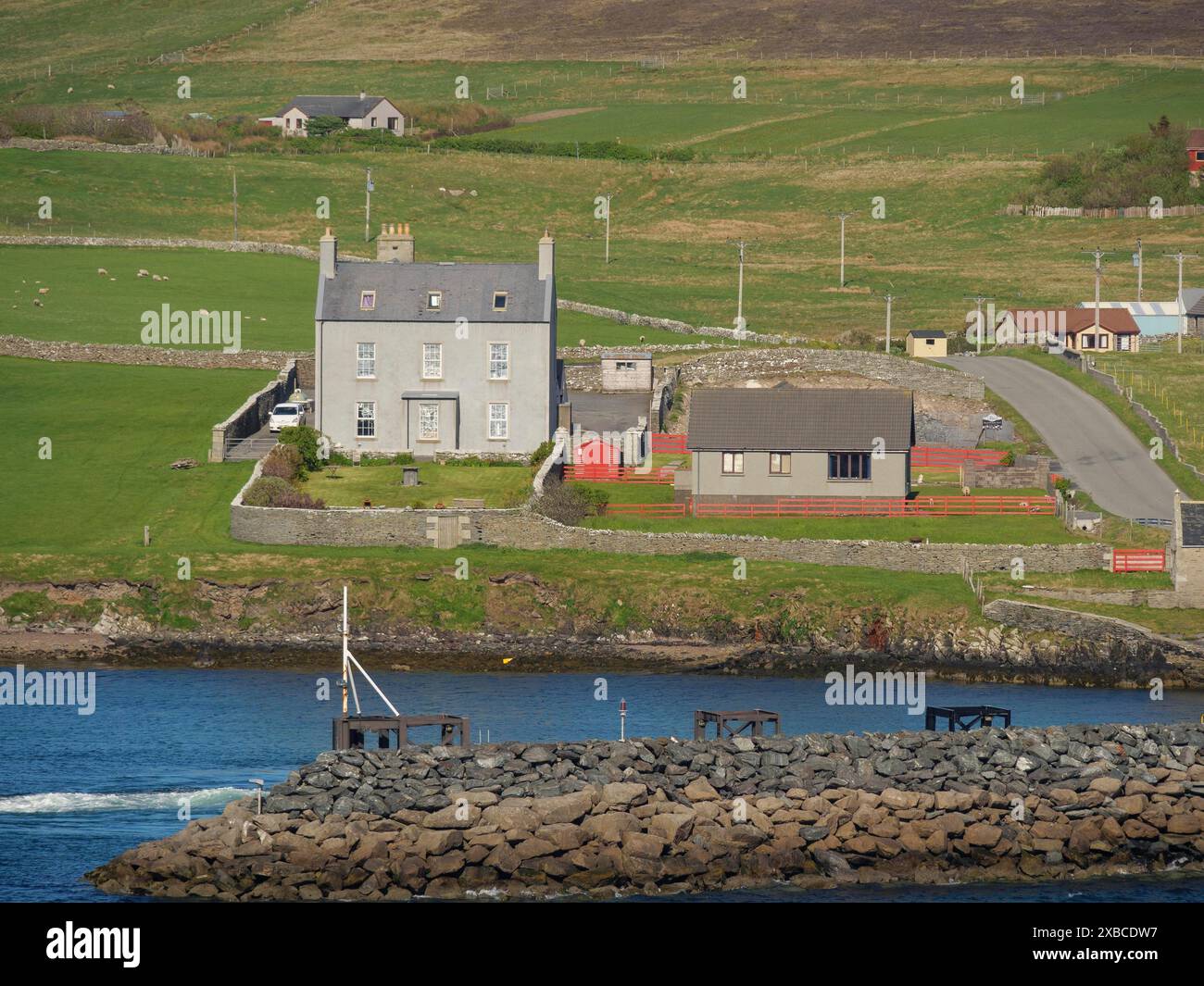 Ein großes Haus am Wasser, umgeben von grünen Hügeln und mehreren Gebäuden, lerwick, shetlands, schottland, großbritannien Stockfoto