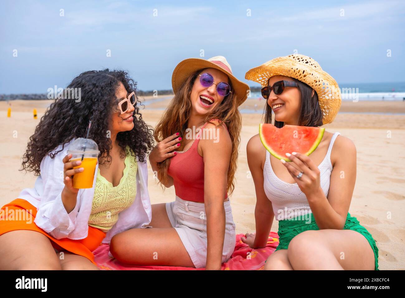 Multiethnische Freunde genießen den Sommer am Strand im Urlaub, draußen lachen auf dem Sand sitzen Stockfoto
