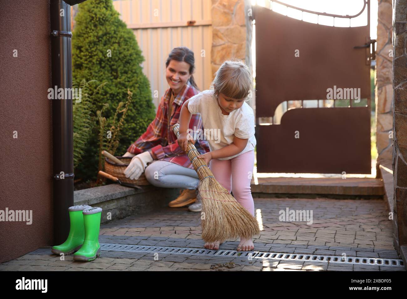 Mutter und ihre süße Tochter putzen zusammen in der Nähe des Hauses am Frühlingstag Stockfoto