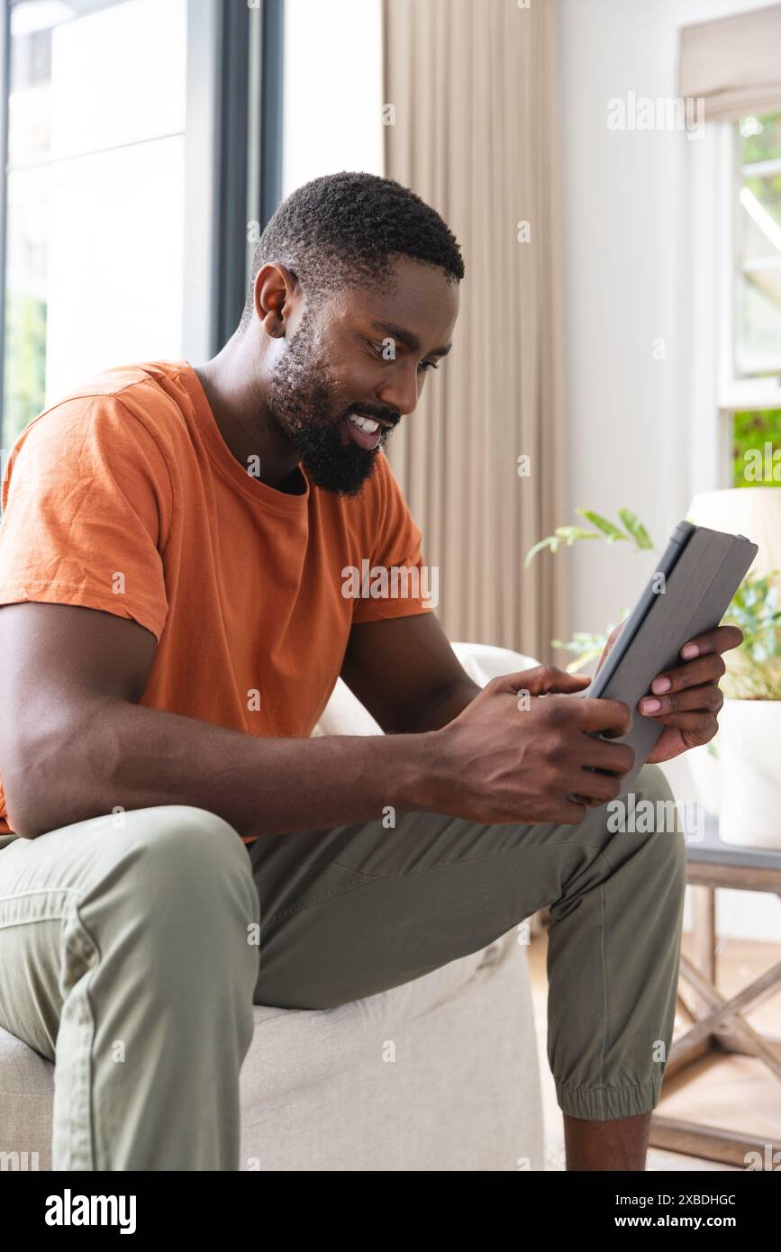 Junger afroamerikanischer Mann lächelt, während er zu Hause ein Tablet benutzt Stockfoto