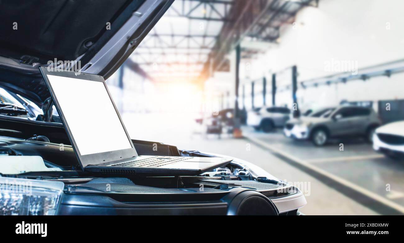 Ein Laptop mit leerem weißen Bildschirm im Motorraum eines Autos in einer Autoreparaturgarage , Servicekonzept für Autowartung Stockfoto