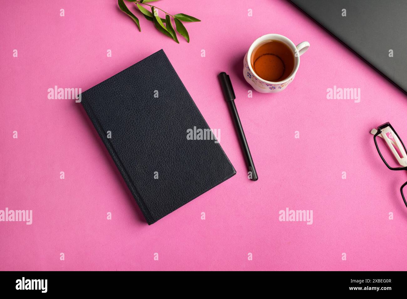 Draufsicht eines Buchmodells auf einem Bürotisch mit Laptop, Stift, Brille, Tasse und Blättern auf rosa Hintergrund Stockfoto