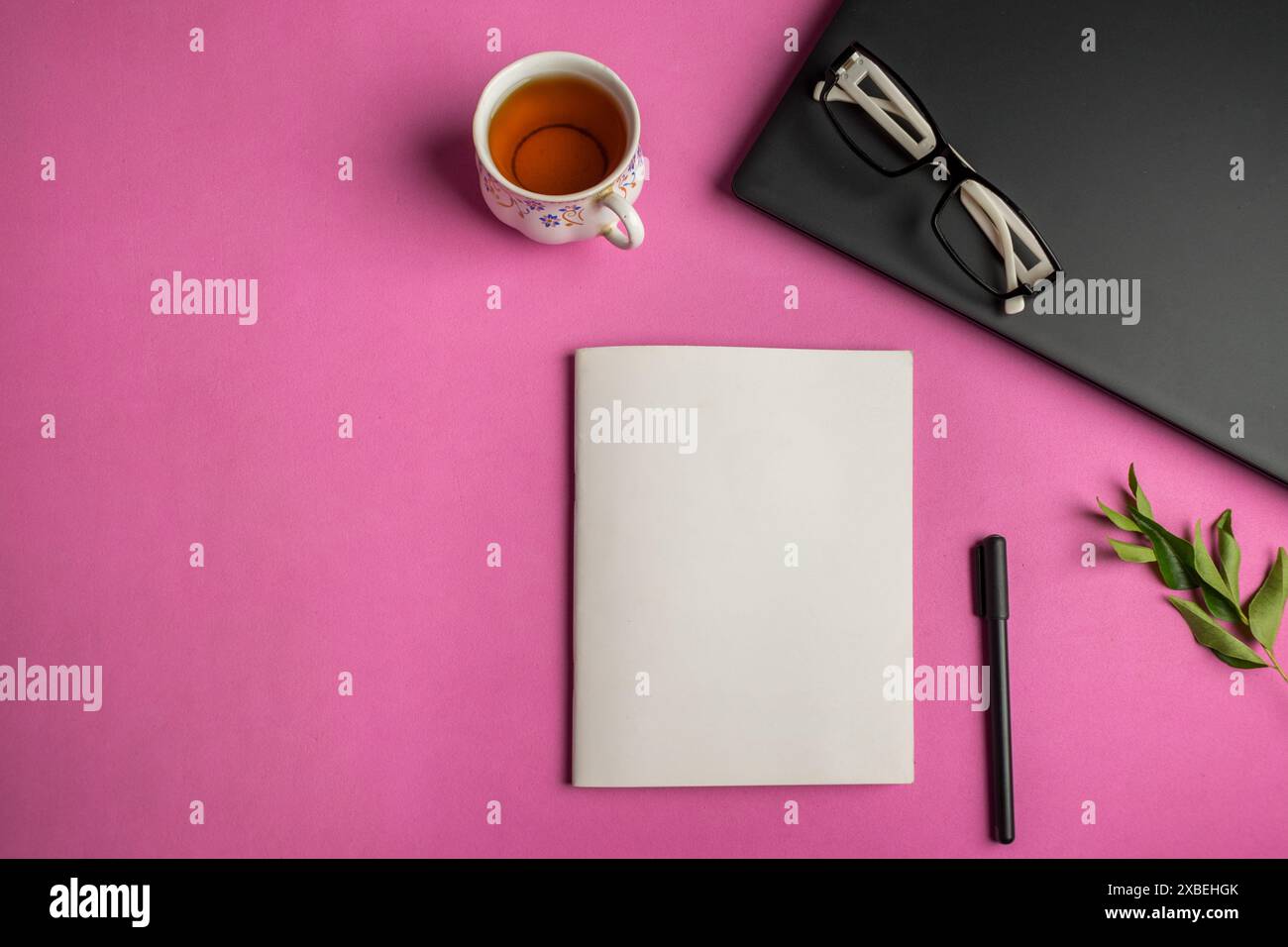 Draufsicht eines Buchmodells auf einem Bürotisch mit Laptop, Stift, Brille, Tasse und Blättern auf rosa Hintergrund Stockfoto