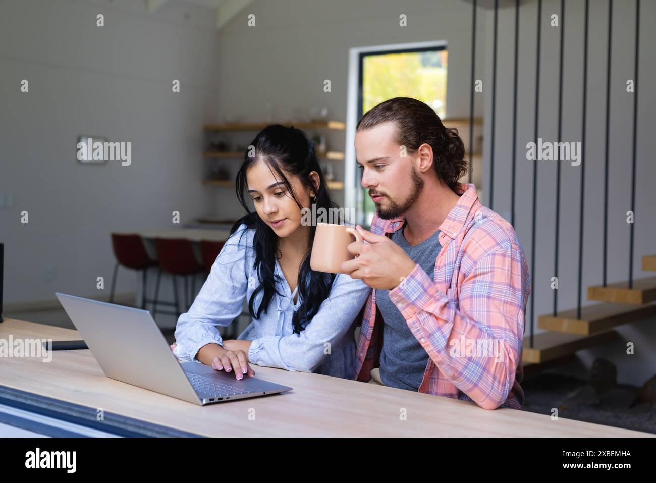 Ein junges, vielseitiges Paar, das zusammen einen Laptop benutzt, ein Mann, der einen Kaffeetasse hält Stockfoto