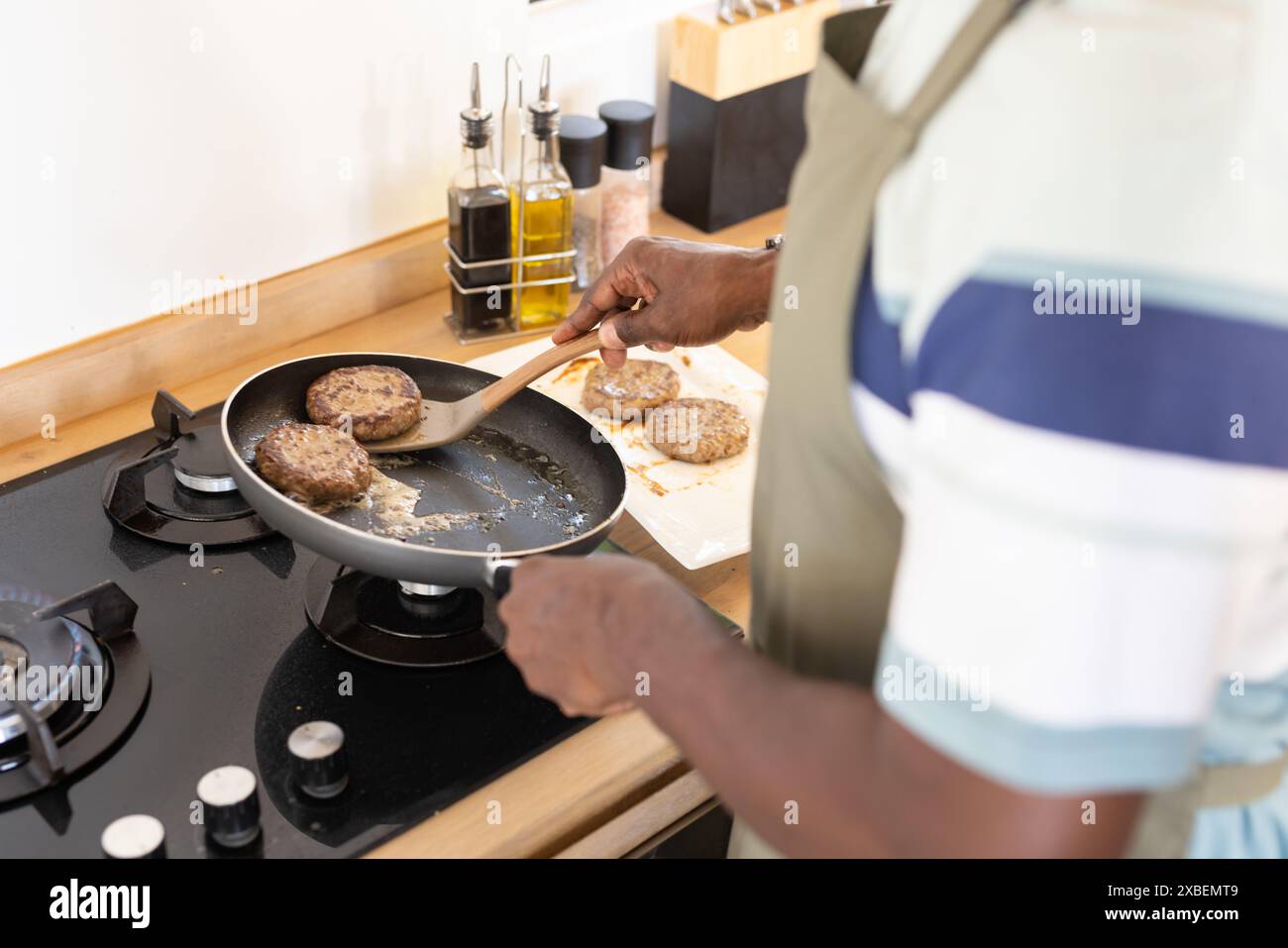 Reifer afroamerikanischer Mann, der Burger in moderner Küche kocht Stockfoto