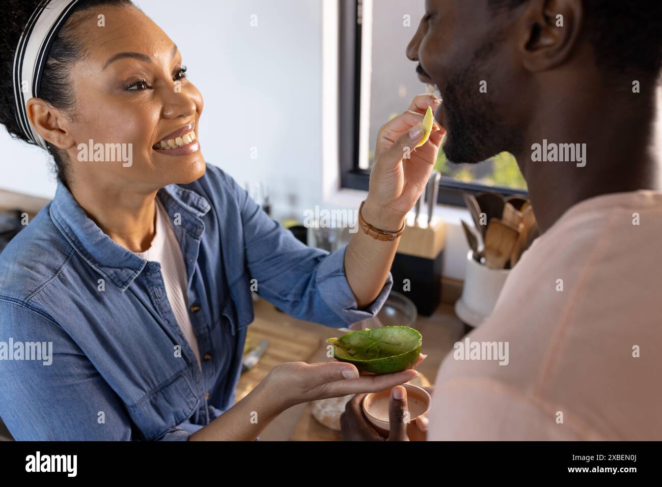 Ein vielseitiges Paar genießt einen Moment in der Küche, die Frau füttert den Mann Stockfoto
