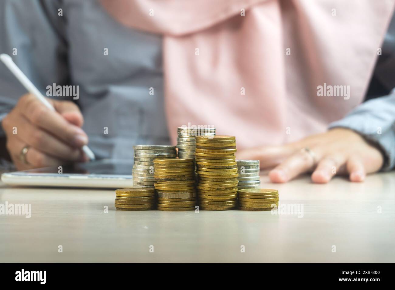 muslimische Geschäftsfrau, die ein Smartphone oder Tablet mit einem Haufen Münze Geld vorne benutzt, Symbol für die Scharia Finanzbank Investmentdividende fro Stockfoto