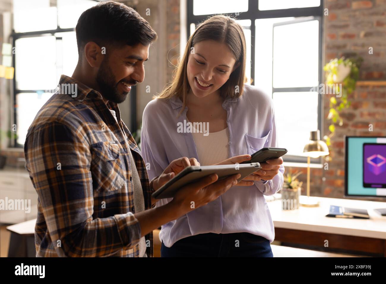 Junge kaukasische Frau, die einem Kollegen im Büro etwas auf dem Tablet zeigt. Moderne Einrichtung und Tageslicht schaffen eine helle und einladende Umgebung Stockfoto