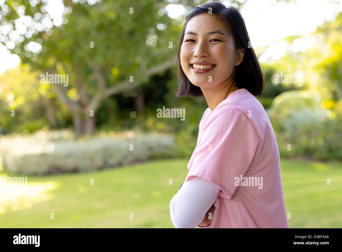 Asiatische Krankenschwester im Gesundheitswesen lächelt im Garten, trägt rosa Hemd, zu Hause Stockfoto