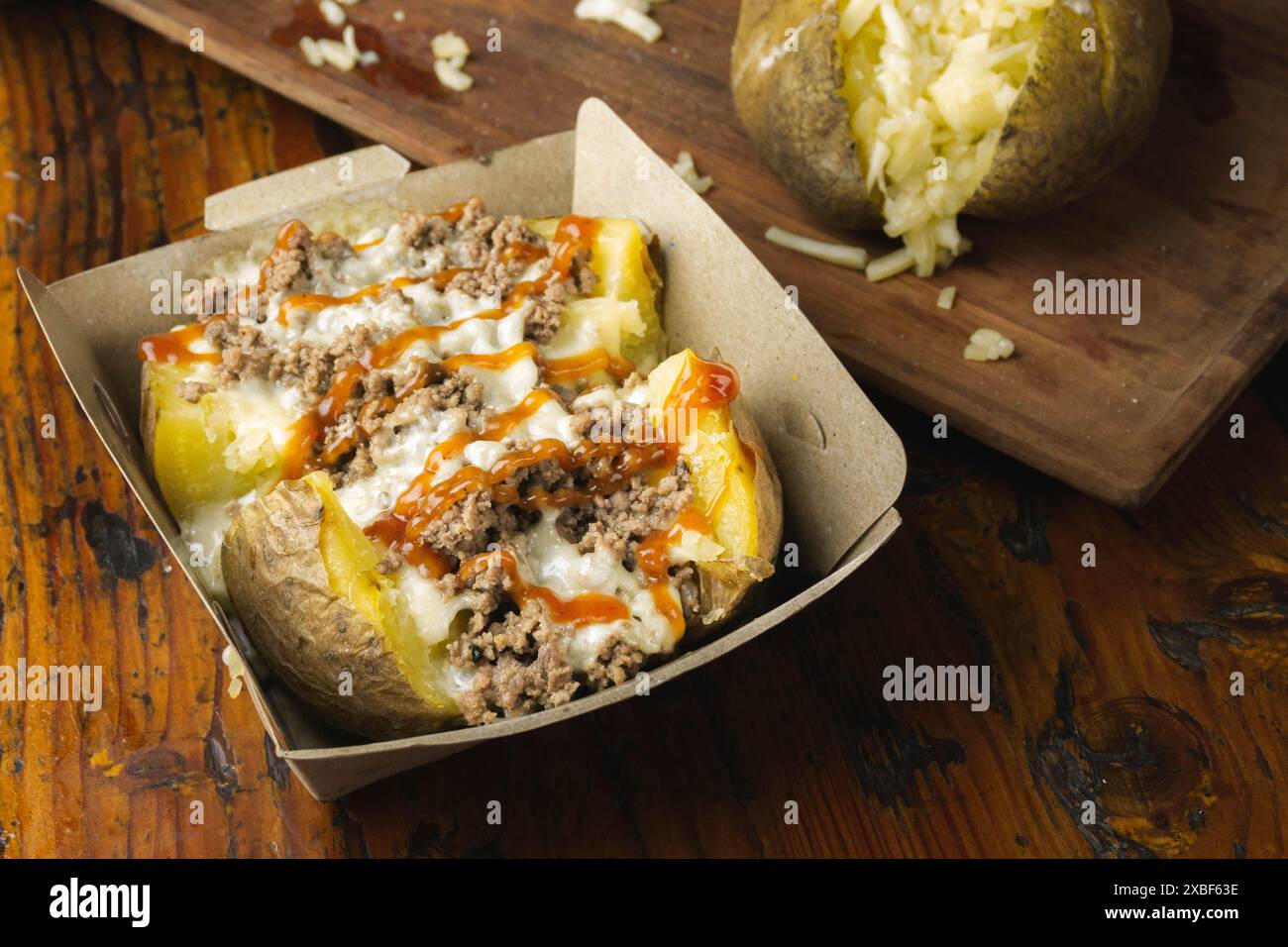 Hausgemachte beladene gebackene Kartoffeln mit Cheddar, Hackfleisch und süß-saurer Sauce Stockfoto