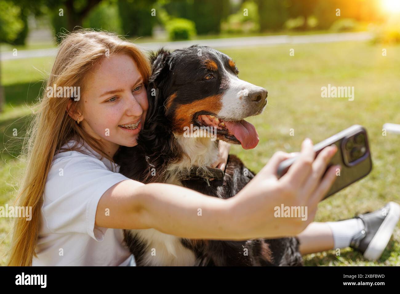 Eine Frau fängt freudig einen Moment ein, indem sie ein Selfie mit ihrem geliebten Hund auf dem Gras macht und beide eine glückliche und ehrliche Geste teilen Stockfoto