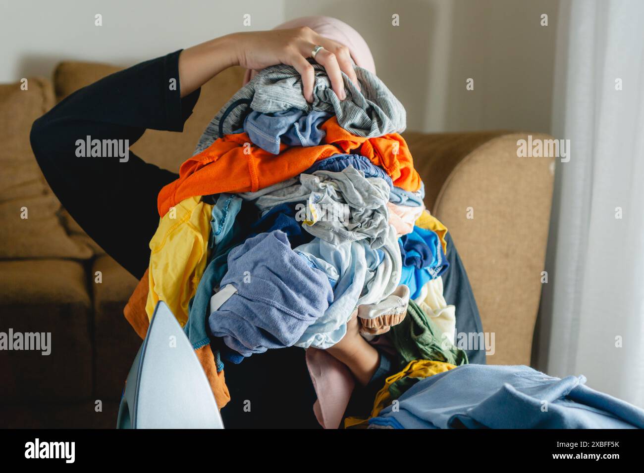 Eine Frau hält einen Stapel faltiger Kleider, die nicht gebügelt wurden Stockfoto