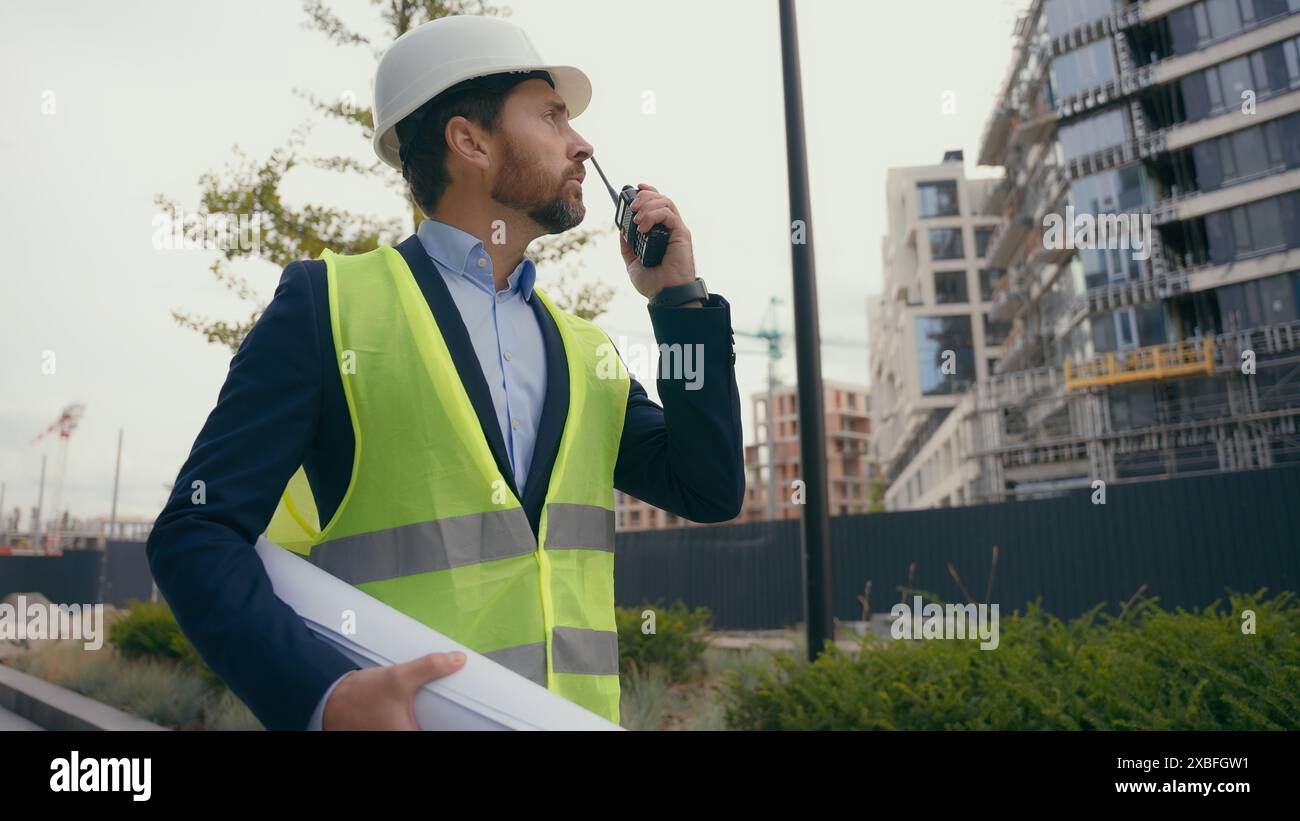 Kaukasischer Bauunternehmer Bauingenieur Elektroinstandhaltungsarbeiter, der einen Bauplan hält, männlich, der auf den Bauerbauer der Stadt blickt Stockfoto