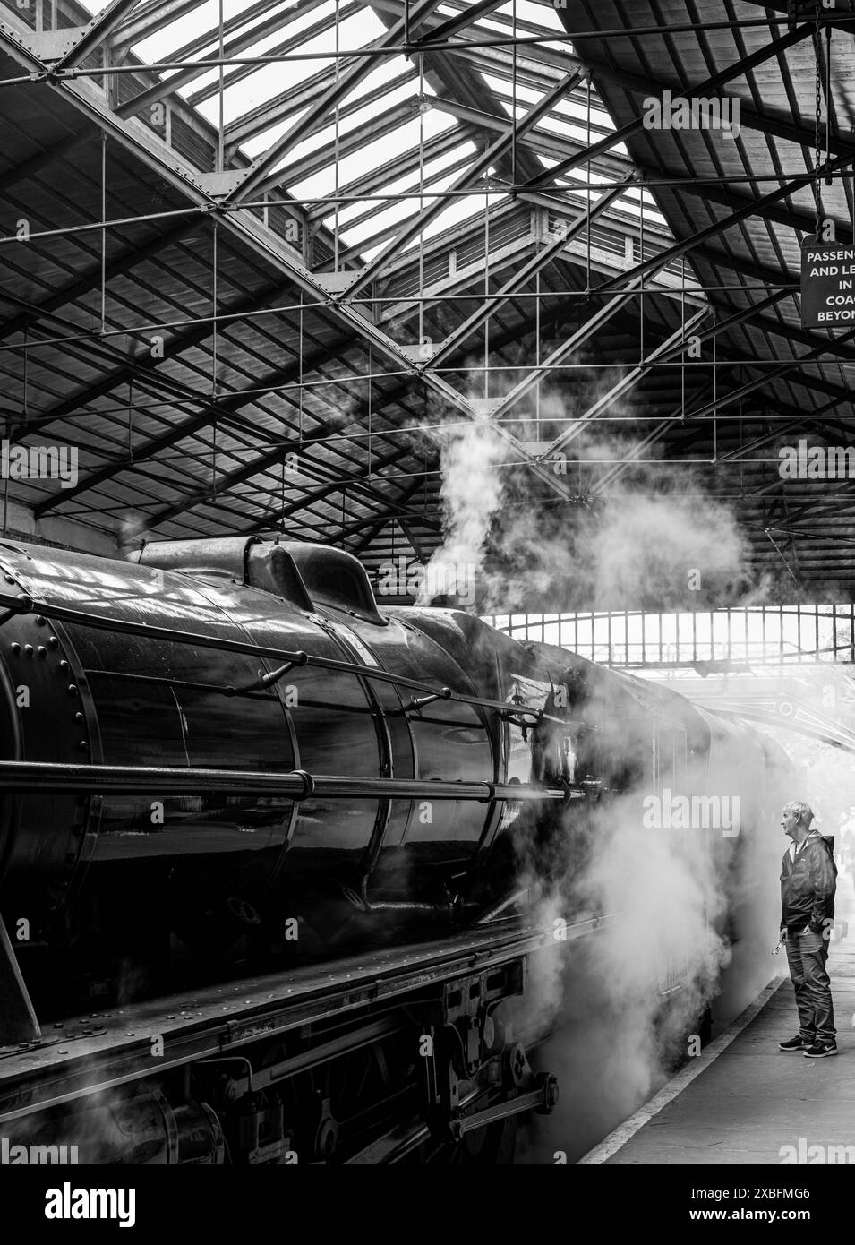 Mann, der auf Bahnsteig eins des Pickering Bahnhofs steht und durch den Dampf schaut. North Yorkshire, England, Vereinigtes Königreich. Schwarzweißfoto. Stockfoto