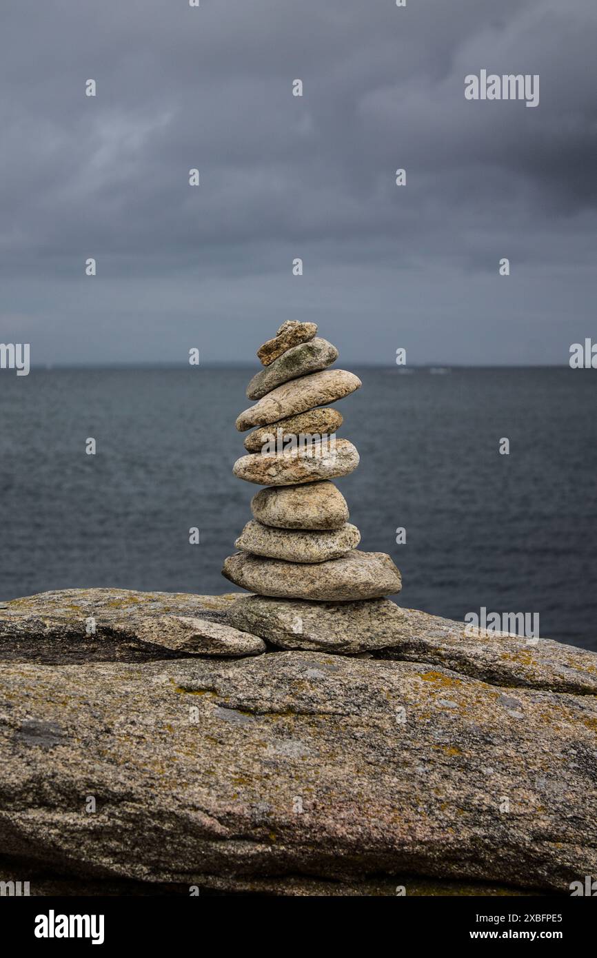 Ein Stapel ausgeglichener Steine an einem felsigen Ufer mit einem bewölkten Himmel im Hintergrund. Stockfoto