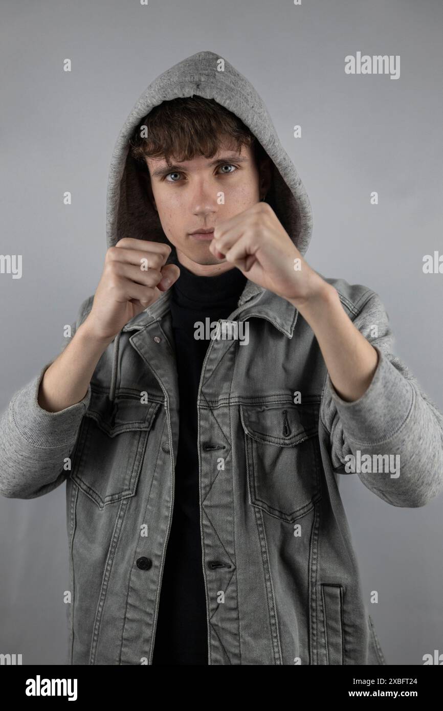 Weißes Hintergrundporträt im Atelier eines jungen Mannes, der Jacke mit Kapuze und Boxen vor der Kamera trägt Stockfoto