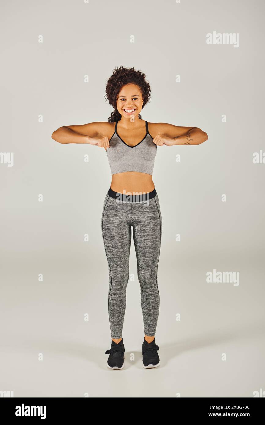 Junge, fitte afroamerikanische Frau, die eine anmutige Pose mit ausgestreckten Armen vor grauem Studio-Hintergrund annimmt. Stockfoto