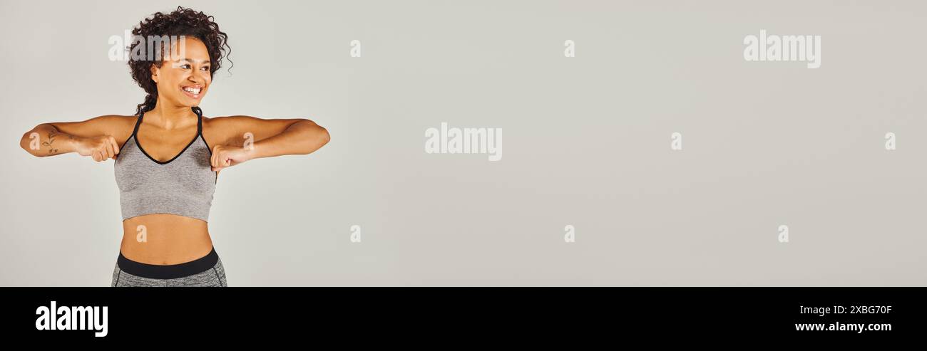 Eine junge Afroamerikanerin in aktiver Kleidung beugt ihre Arme selbstbewusst vor einem weißen Hintergrund. Stockfoto