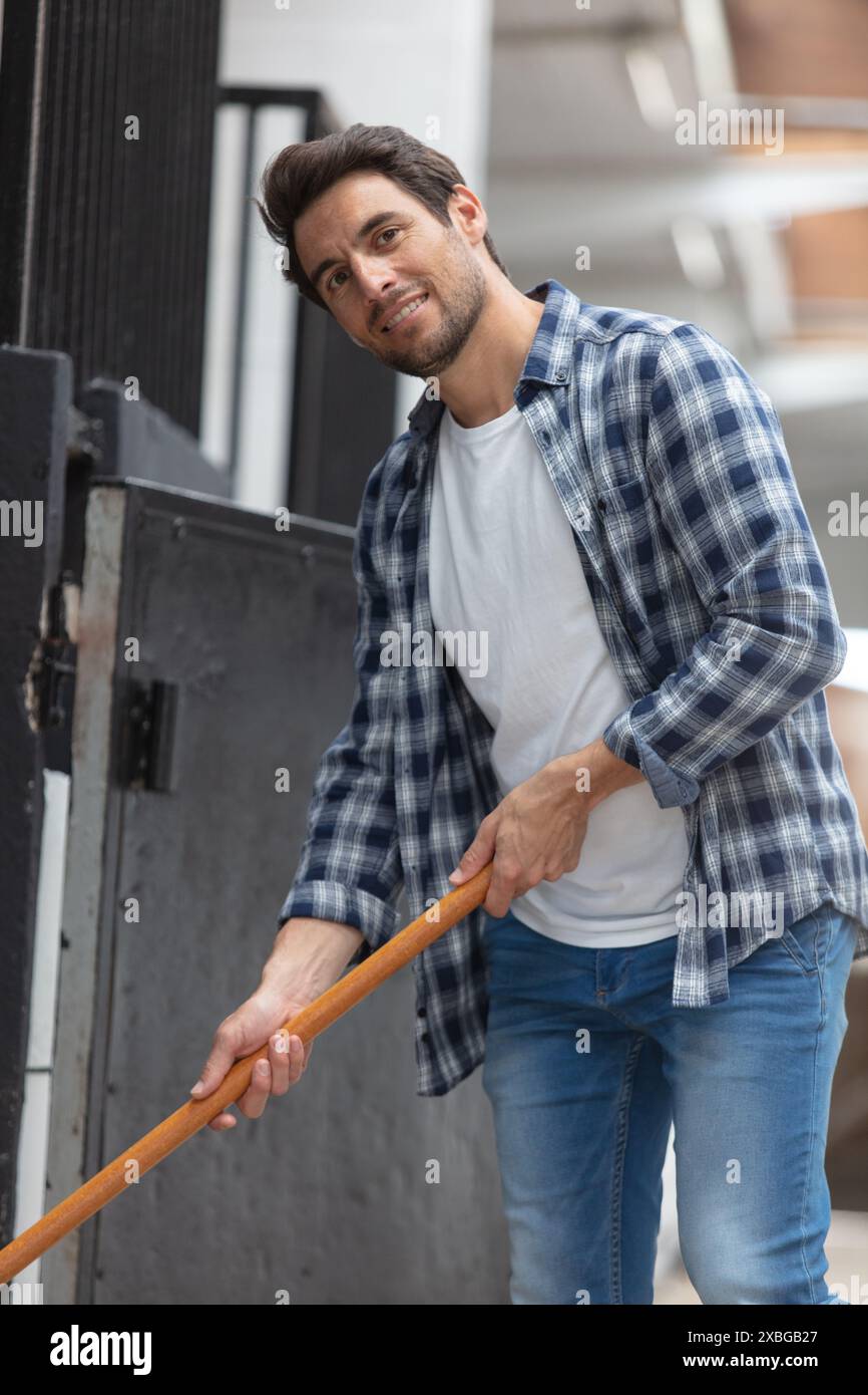 Männlicher Arbeiter, der den Boden in Stallungen reinigt Stockfoto