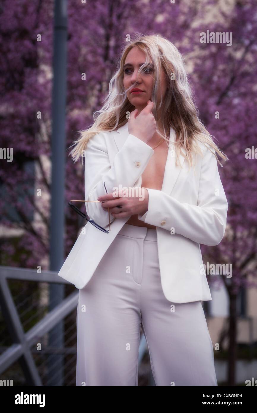 Die blonde Frau steht in Einem 3/4er Schuss, trägt Einen weißen Hosenanzug und hat ihre Jacke offen. Stockfoto