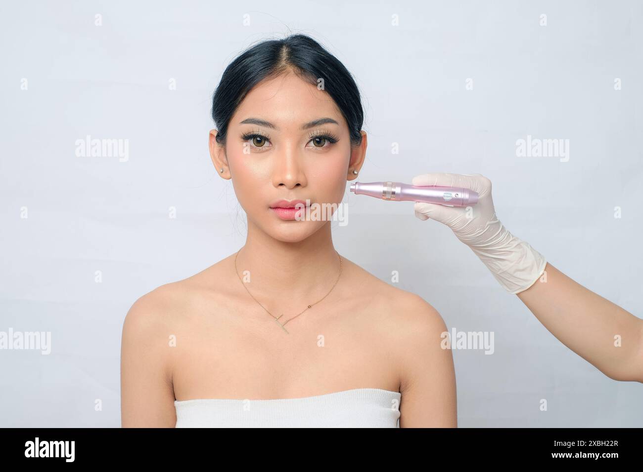 Strahlende asiatische Frau, die Schönheitsbehandlung mit Dermatology Pen zu Hause auf weißem Hintergrund durchführt Stockfoto