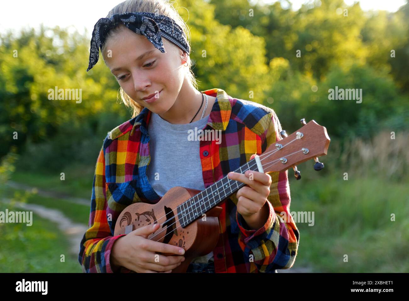 Porträt eines jungen Mädchens, das draußen Ukulele spielt und Musik genießt. Mädchen spielt draußen Gitarre, Ukulele in der Hand, Porträt. Materialien für Musikunterricht Stockfoto