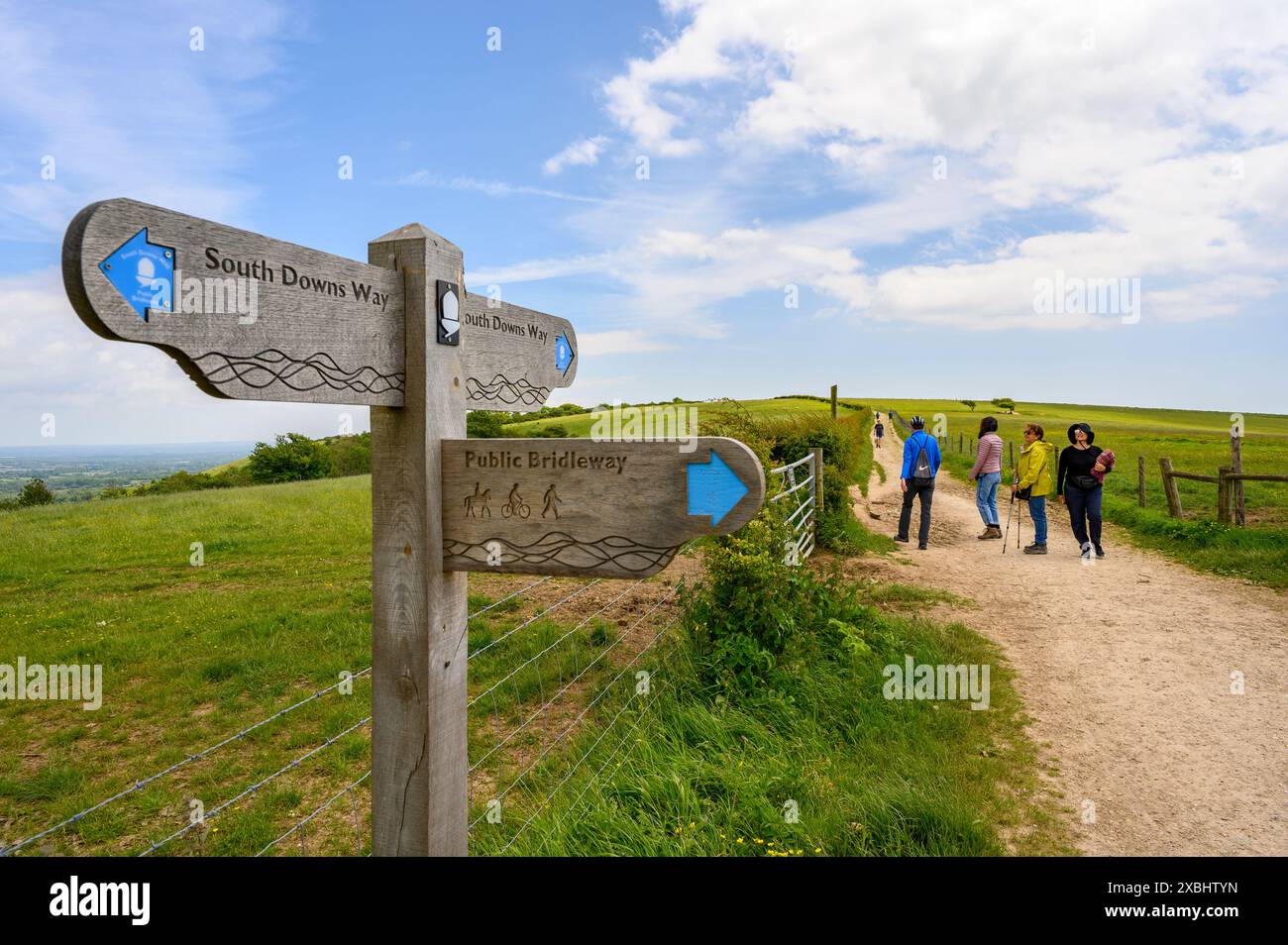 Hölzerne Wegweiser mit drei Wegbeschreibungen auf dem South Downs Way mit einer Gruppe von Wanderern in der Nähe von Clayton, West Sussex, England. Stockfoto Hölzerne Wegweiser mit drei Wegbeschreibungen auf dem South Downs Way mit einer Gruppe von Wanderern in der Nähe von Clayton, West Sussex, England. Stockfoto