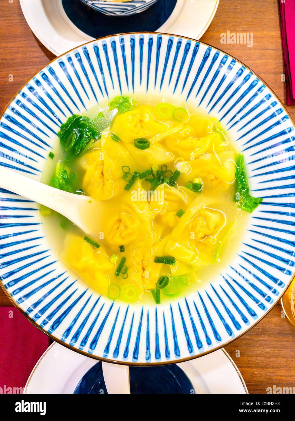 Eine Schüssel Wonton-Suppe mit Gemüse, mit gelben Wontons, frischen grünen Zwiebeln und Blattgemüse. Stockfoto