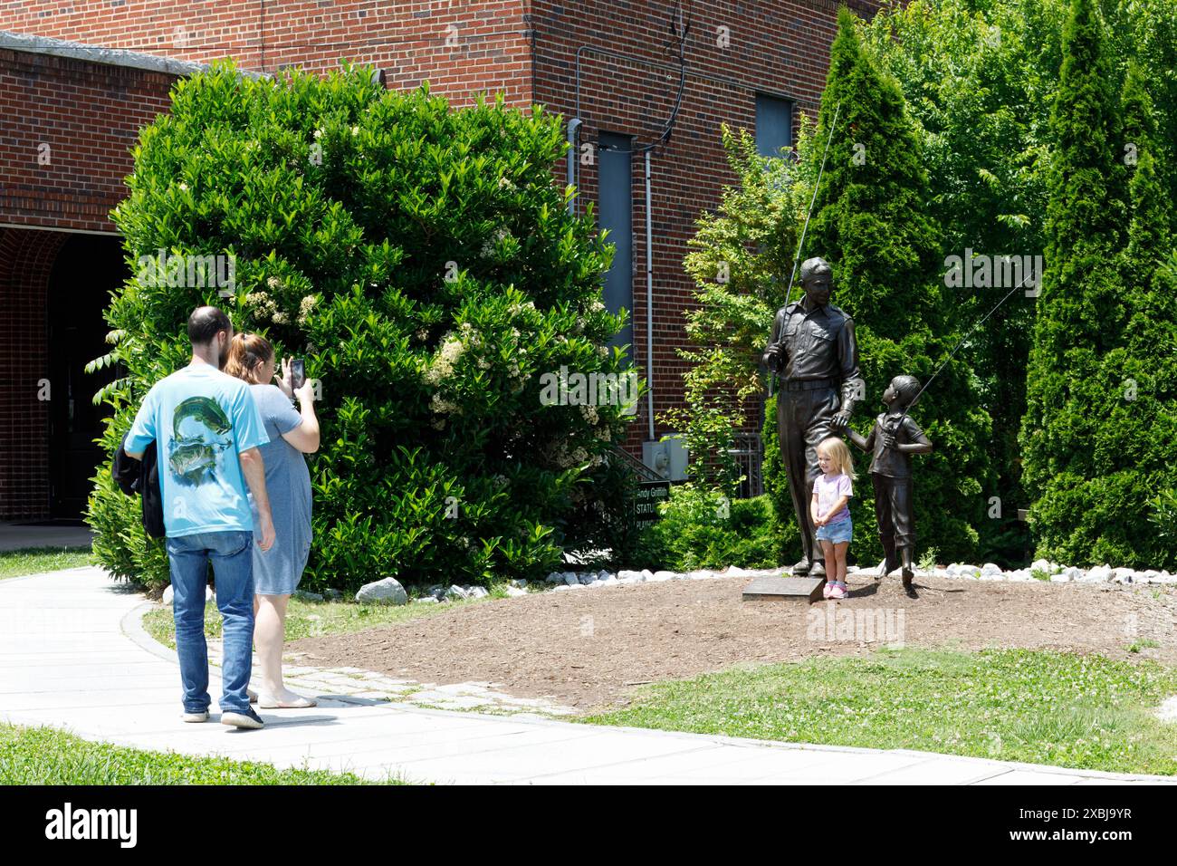 Mt. Airy, NC, USA-1. Juni 2024: Ein Paar macht ein Foto ihrer kleinen Tochter, die vor der Skulptur von „Andy and Opie“ auf der Gros steht Stockfoto