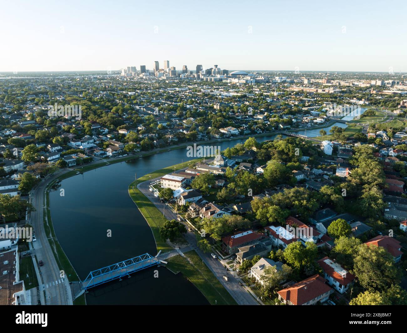 Aus der Vogelperspektive auf das historische Bayou St. John, das sich durch ein üppiges Viertel von New Orleans schlängelt, mit der Skyline der Stadt in der Ferne. Stockfoto