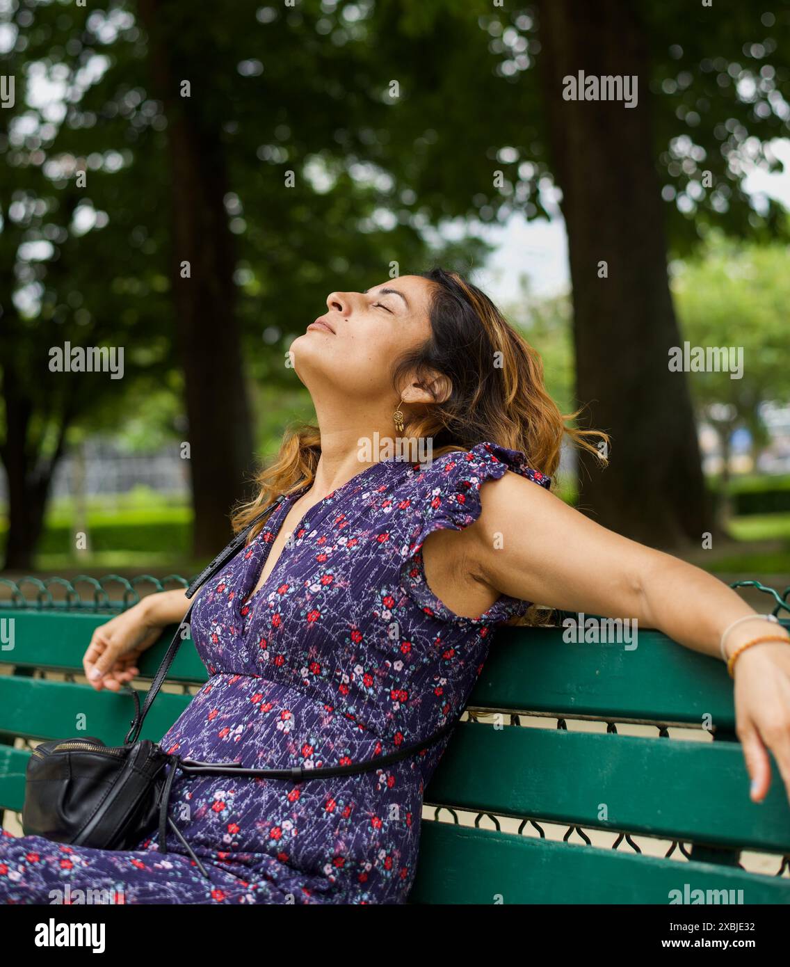 Eine hübsche hispanische Frau, die sich auf einer Bank in einem Park in Paris entspannt. Kopierbereich Stockfoto