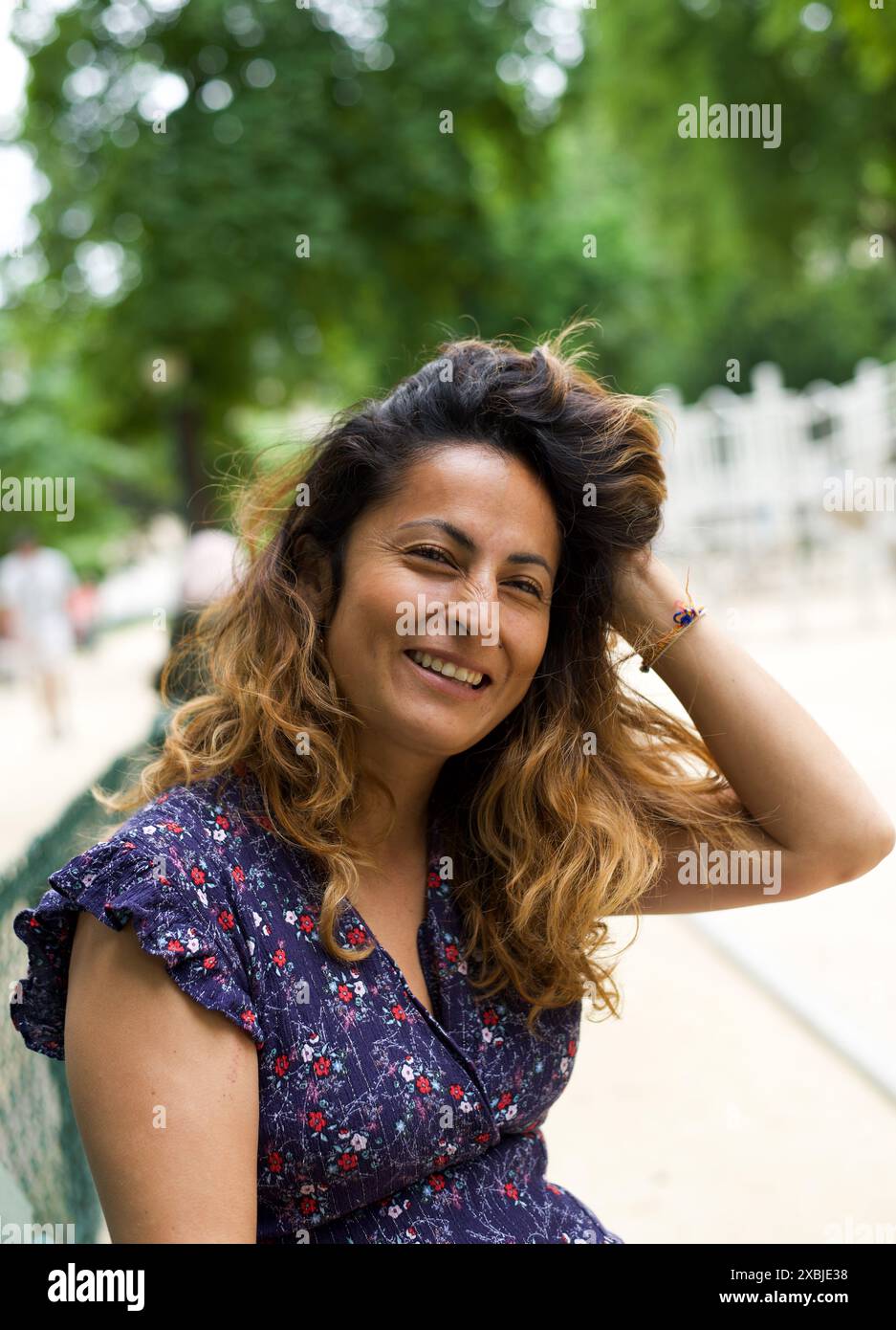 Porträt einer schönen hispanischen Frau, die in die Kamera lächelt, während sie in einem Park in Paris sitzt Stockfoto