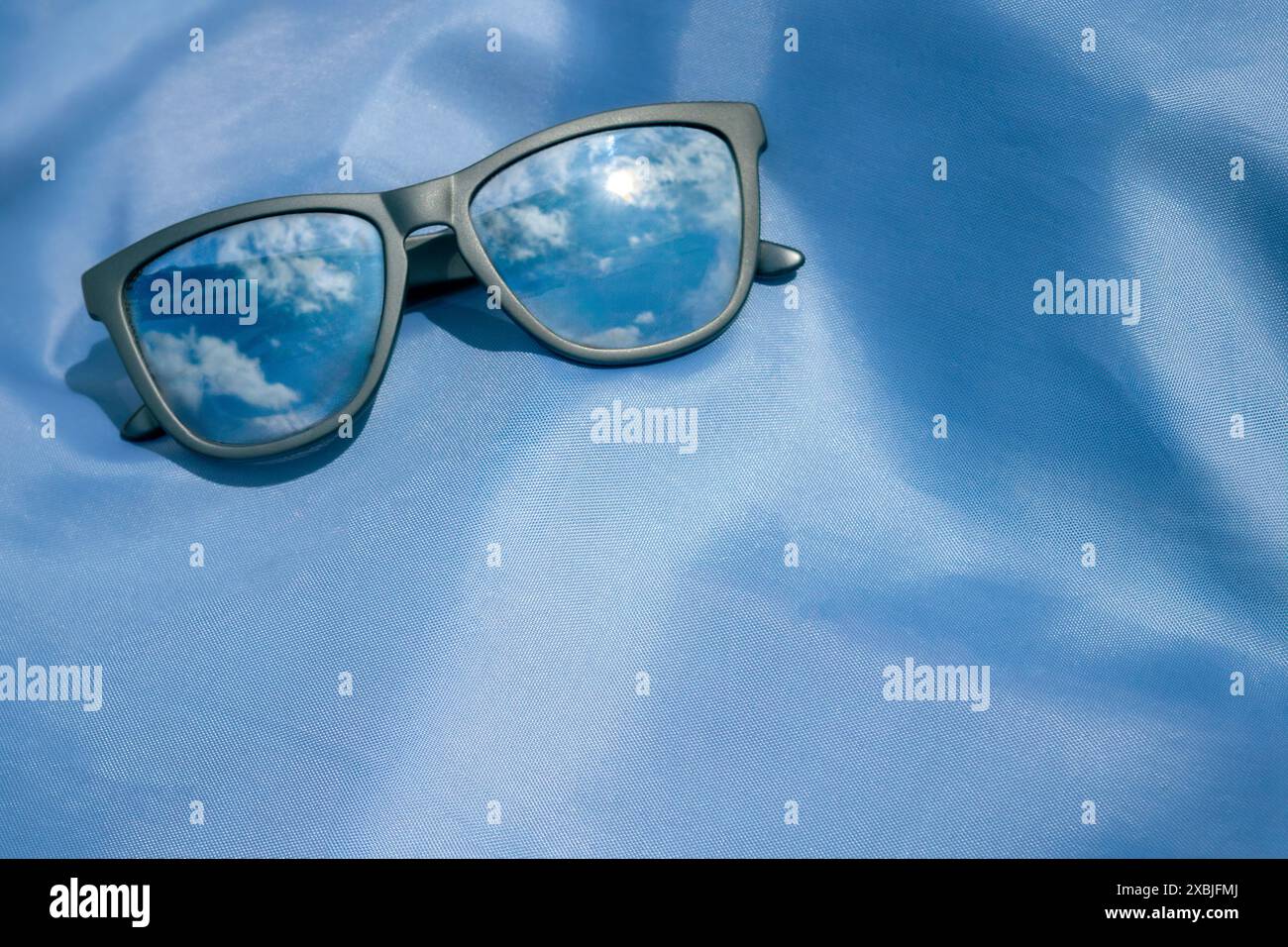 Stilvolle schwarze Sonnenbrille reflektiert den blauen Himmel und das Sonnenlicht auf einem leuchtend blauen Hintergrund mit leerem Platz für Text. Sommermode Stockfoto