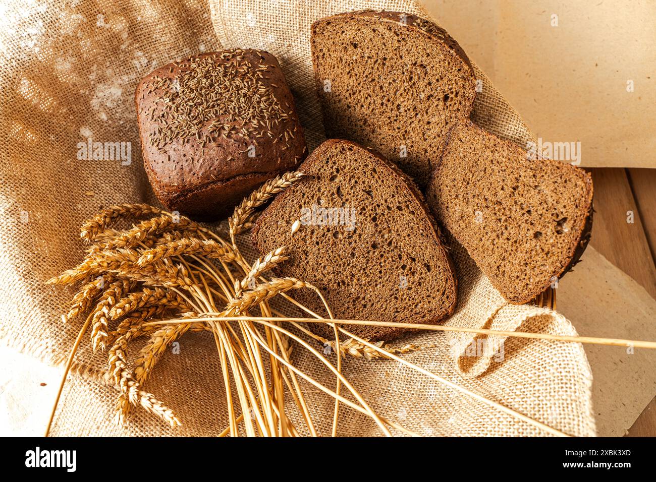 Ein Brotlaib aus schwarzem Borodino und geschnittene Scheiben auf Leinwand und ein Ohr aus Roggen. Hochwertige Fotos Stockfoto