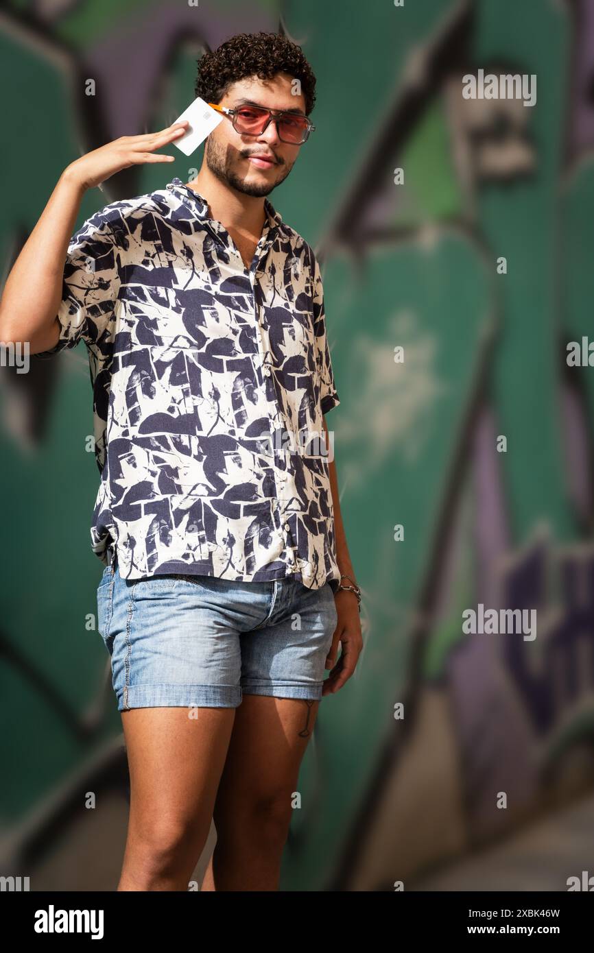 Ein junger Mann mit Sonnenbrille zeigt seine Kreditkarte an einem sonnigen Tag. Mode, Finanzen, urbaner Lebensstil. Stockfoto