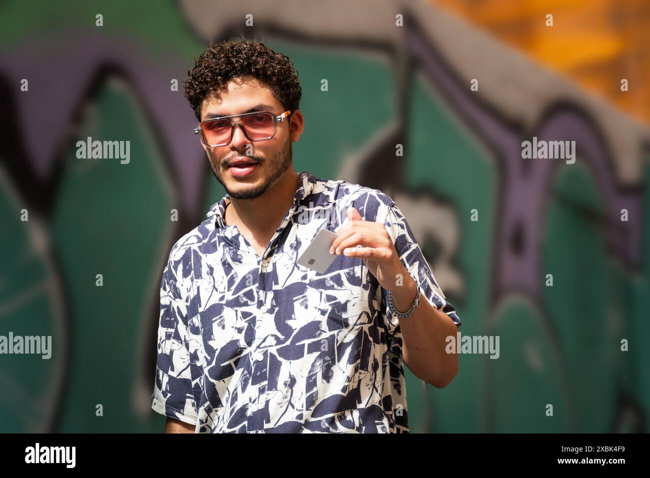Ein junger Mann mit Sonnenbrille zeigt seine Kreditkarte an einem sonnigen Tag. Urbane Mode, Finanzen, sonniger Tag Stockfoto