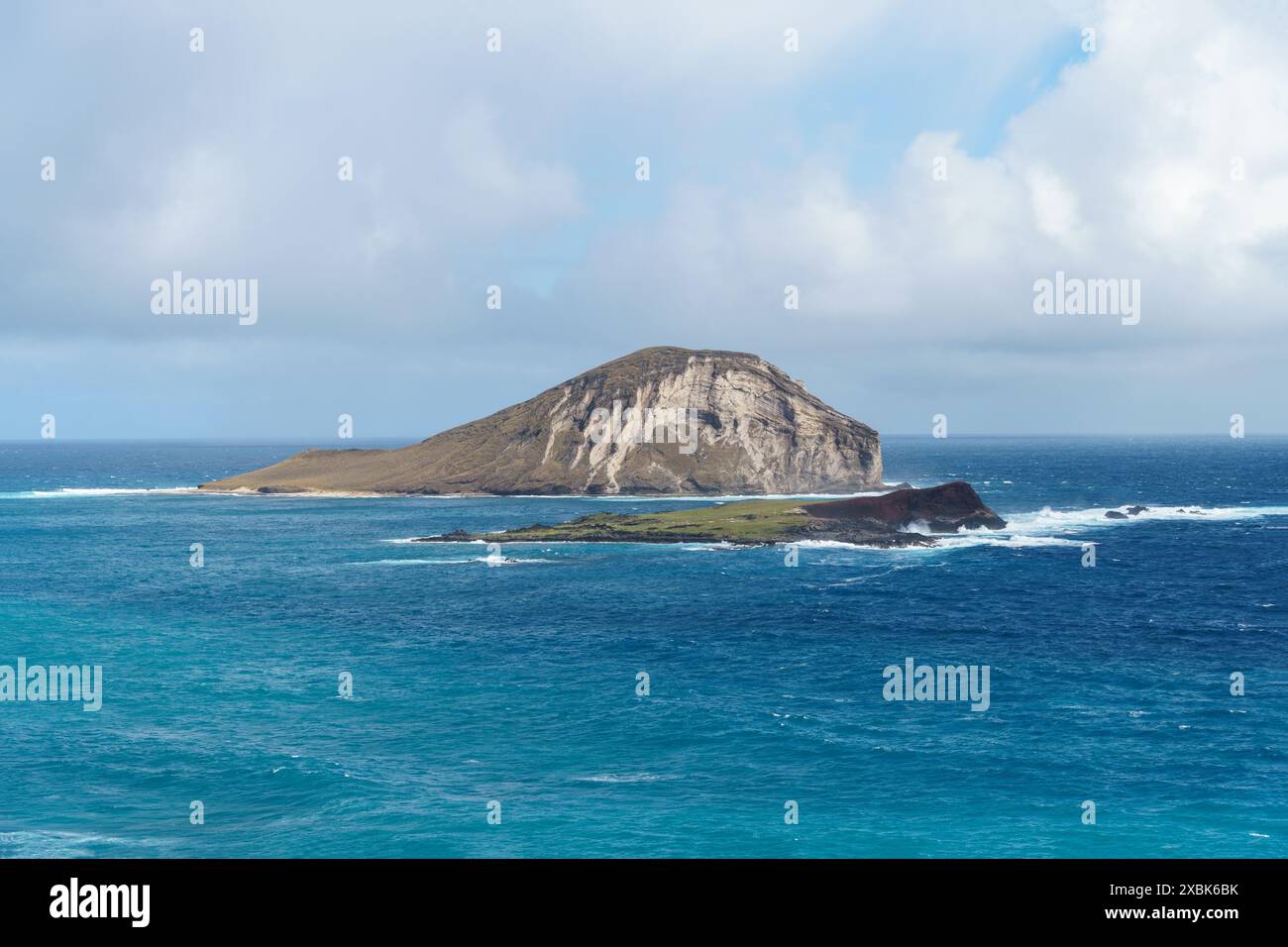 Eine winzige Insel, eingebettet in die weite Weite des Ozeans, umgeben von Wasser, Wolken und Himmel. Es bildet eine atemberaubende natürliche Landschaft am Horizont, bl Stockfoto