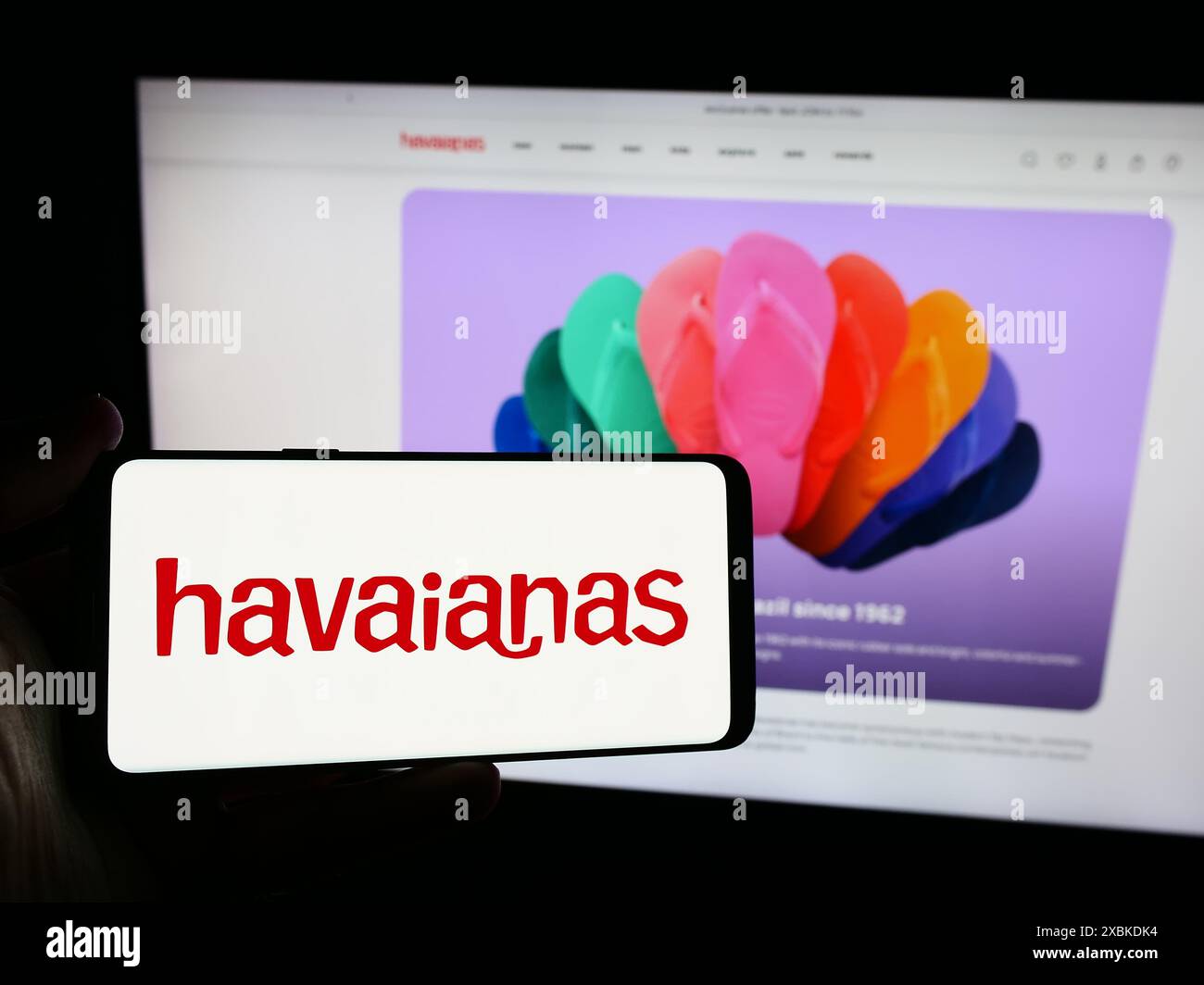 Person mit Smartphone und Logo des brasilianischen Flipflop-Herstellers Havaianas vor der Website. Schwerpunkt auf dem Display des Telefons. Stockfoto